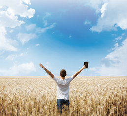 A person stands in front of a field with their arms open wide, open to the possibilities of a strong agriculture future.