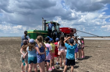 Elementary students gather around a tractor in the field to learn about what it is used for.